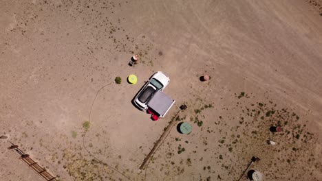 Top-down-view-of-a-white-SUV-at-an-off-the-grid-campsite-in-the-desert,-aerial