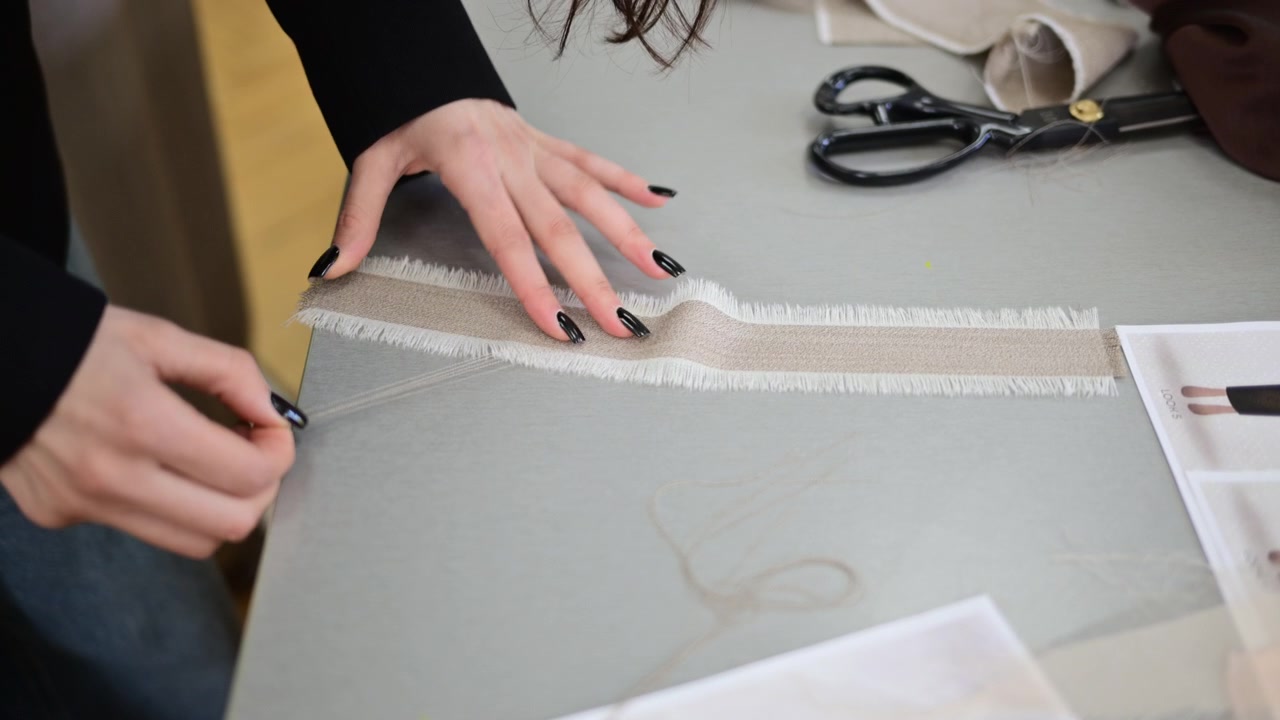 Hands measuring and aligning fabric strips on a design table, preparing materials for garment construction