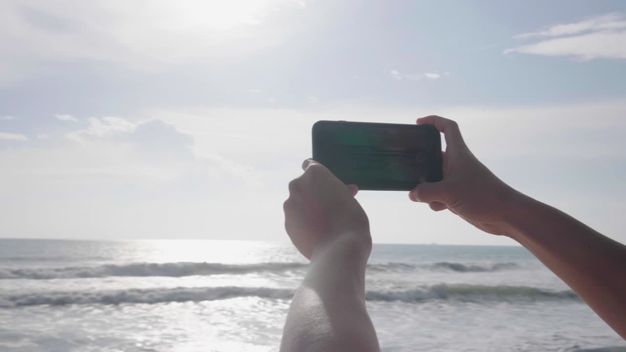 휴가 중 바다 근처의 해변에서 해가 지면 스마트폰으로 손으로 사진을 찍습니다.