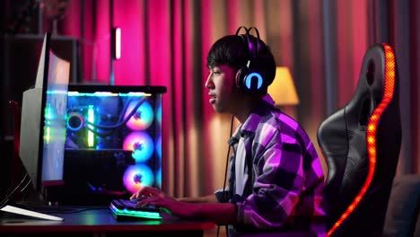 serious asian teen boy gamer playing video game on computer