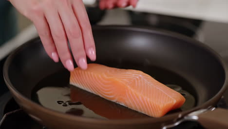 placing raw salmon in a frying pan to cook
