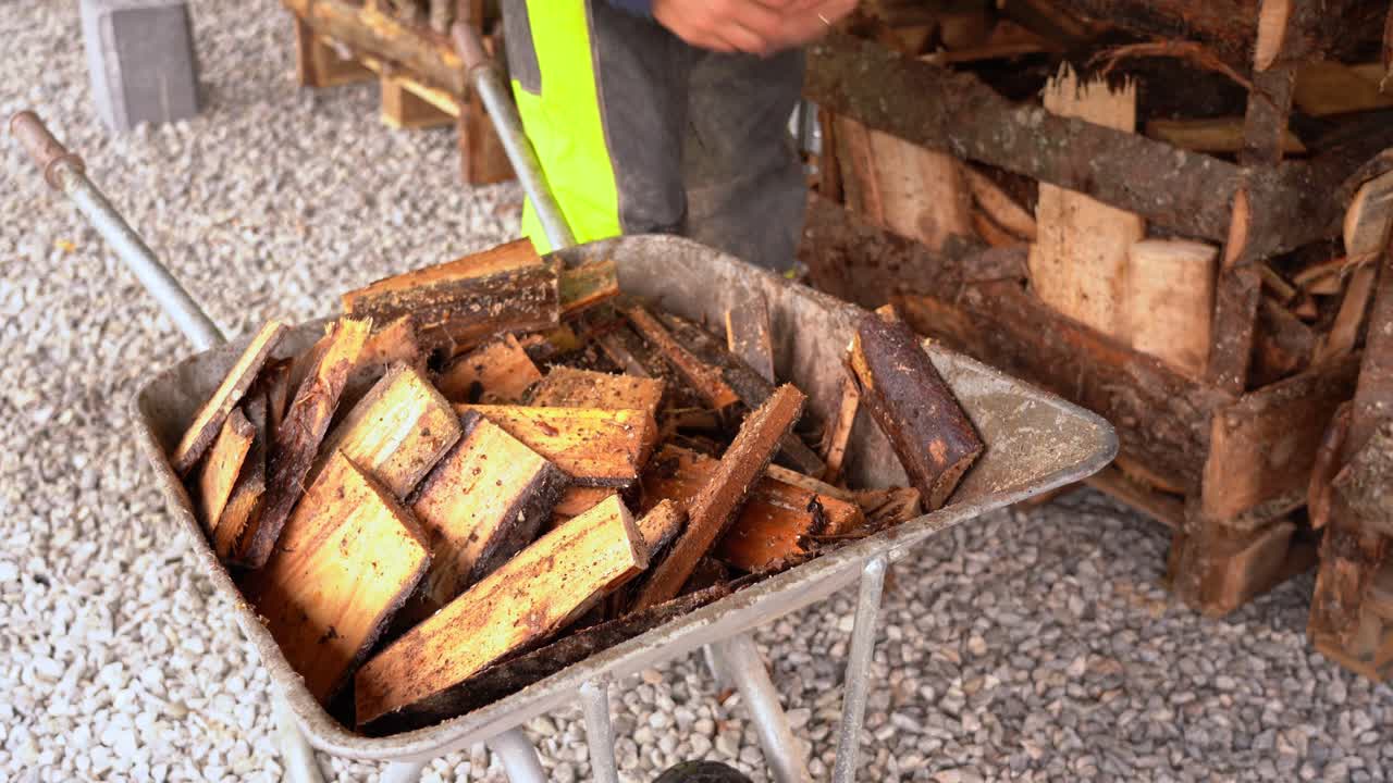 외바퀴 손수레에서 갓 자른 장작 조각을 가져다가 저장 및 건조를 위해 쌓이는 남성 노동자의 손 - 외바퀴 손수레의 근접 촬영