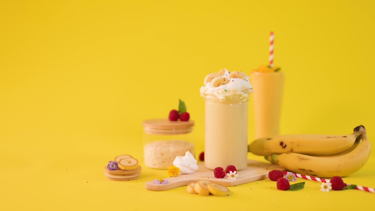 Una mano umana decora un cremoso smoothie alla banana con una cannuccia e un ombrellino su uno sfondo giallo brillante in studio