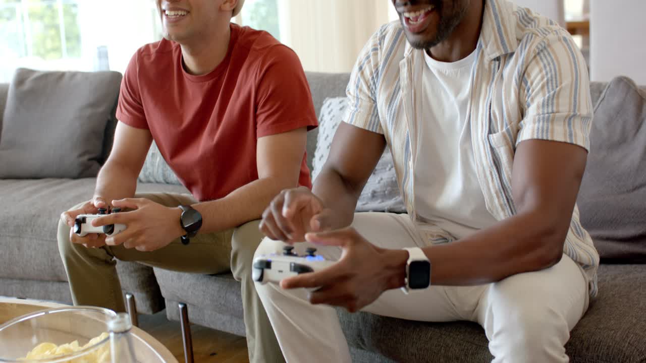 Two male friends grasping controllers and laughing while competing console game on sofa for fun