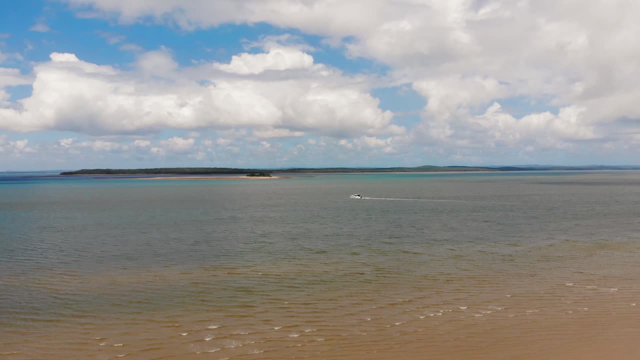 empuje lento hacia un barco que navega suavemente entre dos islas tropicales en un día magnífico y soleado donde el cielo azul presenta muchas nubes blancas, grandes y esponjosas que flotan sobre su cabeza