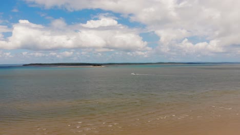 slow push towards a boat gently sailing between two tropical islands on a gorgeously sunny day where the blue sky above features many large, fluffy, white clouds that float overhead