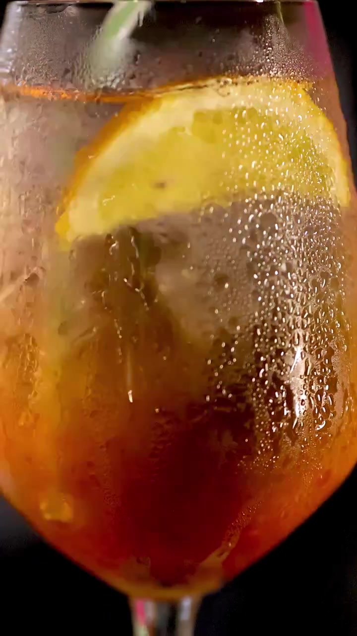 Nahaufnahme eines Negroni-Cocktails, der mit Eis in einer schwach beleuchteten Bar gerührt wird
