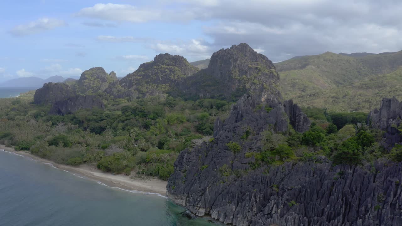 fotografía cinematográfica de un avión no tripulado de una costa con formación de rocas y una playa en una zona tropical durante el día