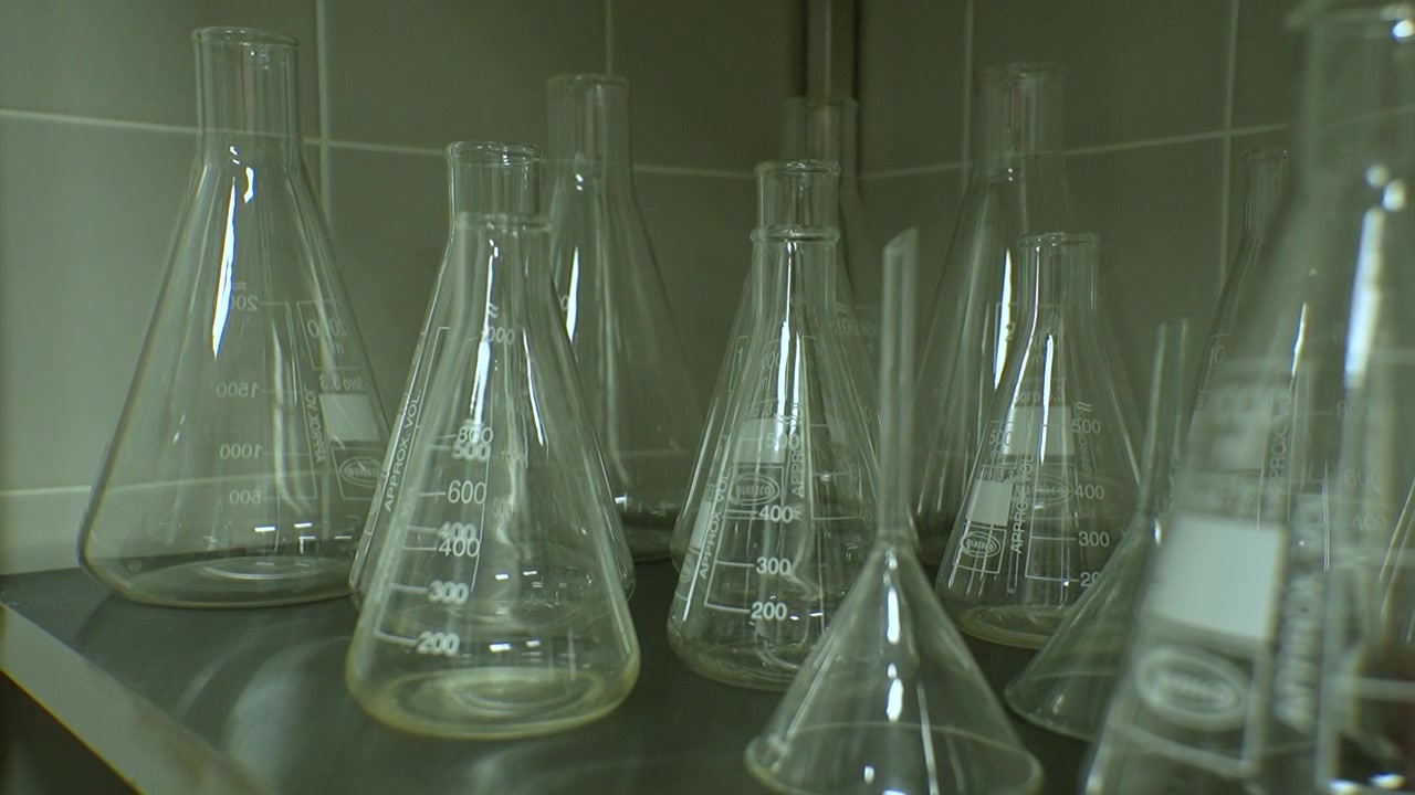 A set of transparent test tubes filled with various liquids, alongside a digital scale, neatly arranged on a laboratory shelf. Ample copy space available.