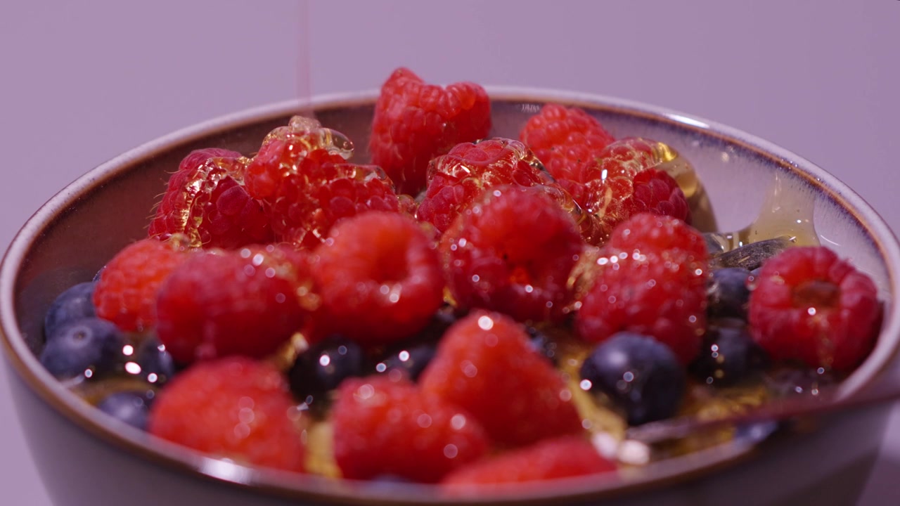 Dripping some hone on some berries in a bowl.