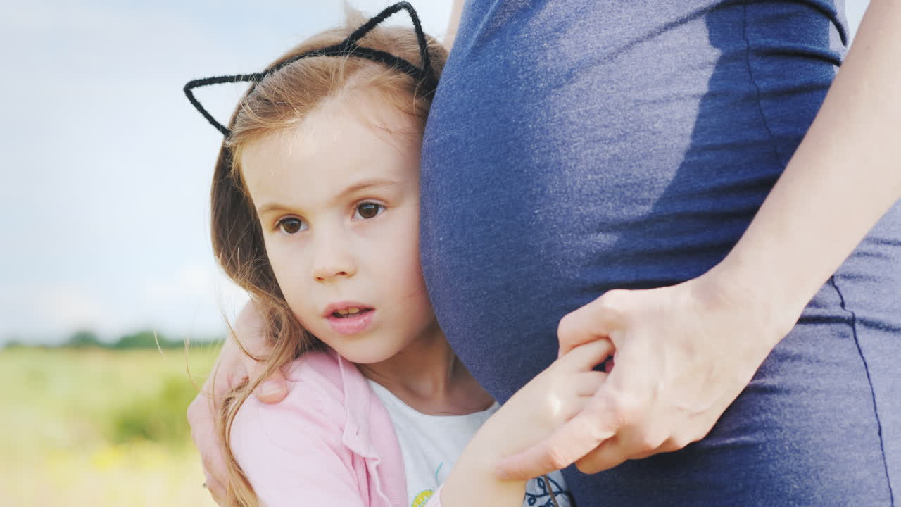 어린 소녀가 임신한 엄마의 배에 귀를 대고 있다