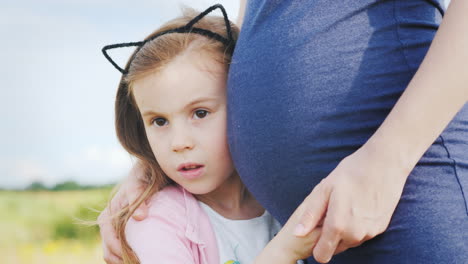 a little girl presses her ear to the belly of a pregnant mother