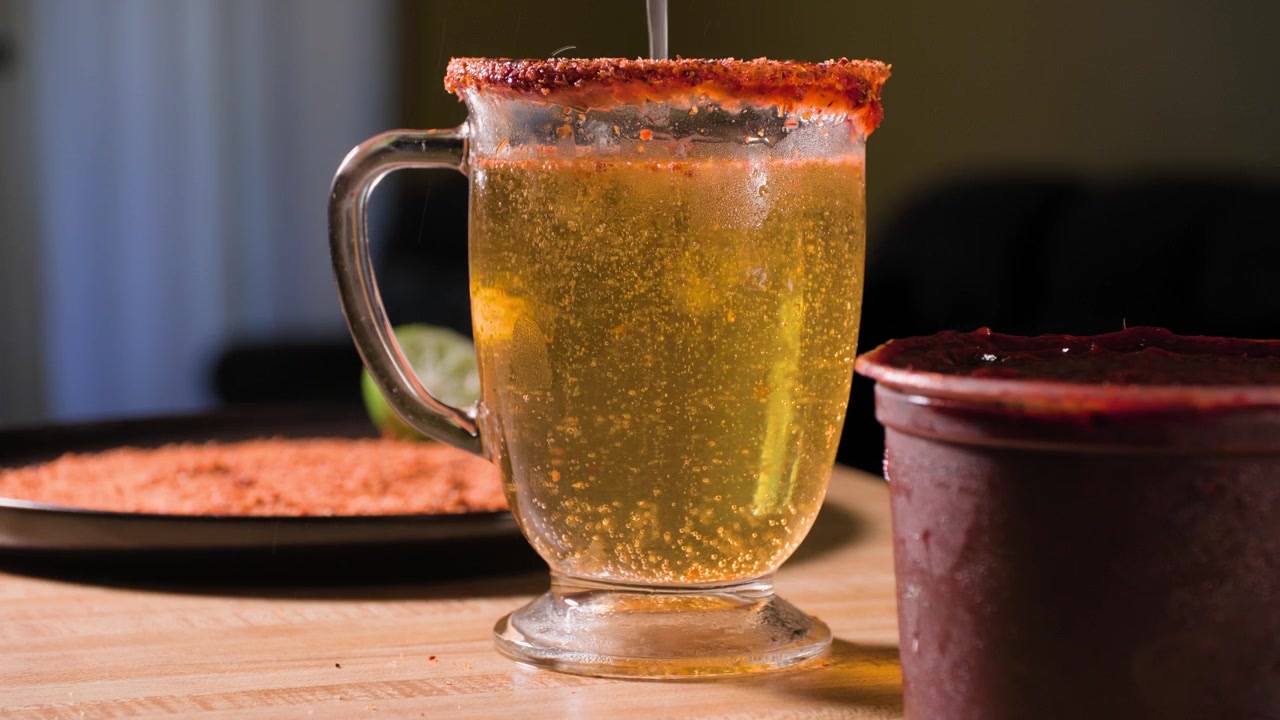 Riprese ravvicinate di un uomo che aggiunge lime fresco e condimento Tajin a un bicchiere di birra mentre prepara una gustosa bevanda michelada al chamoy fatta in casa