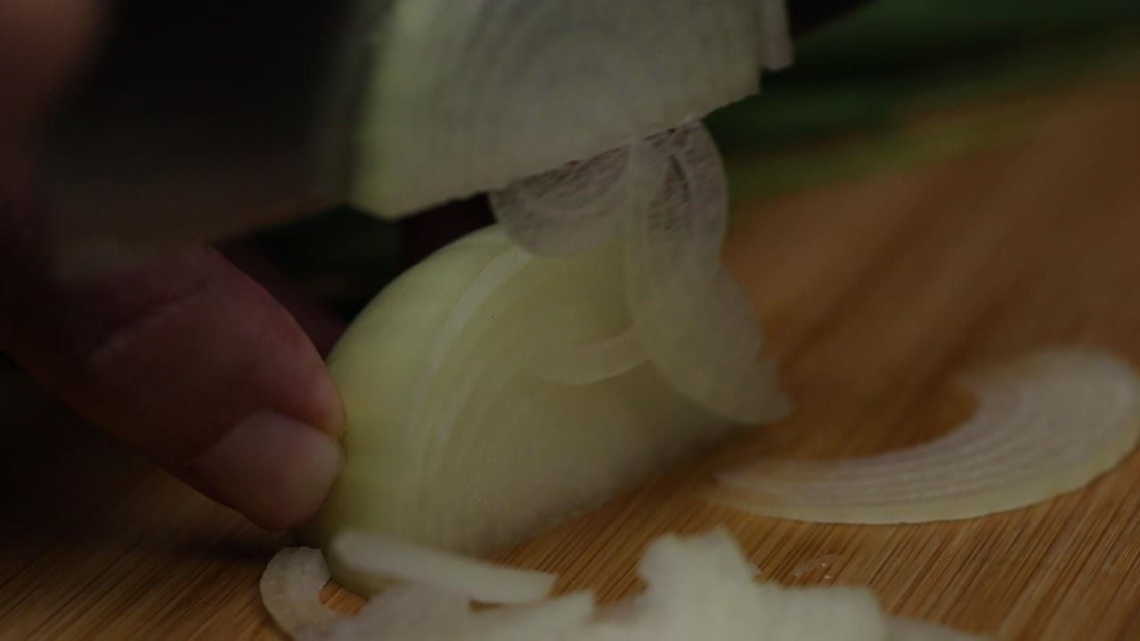 Slow motion close up macro shot of slicing onion in thin pieces, chef preparing vegetables to cook