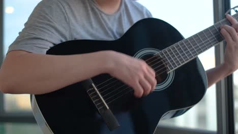 man playing acoustic guitar by the window