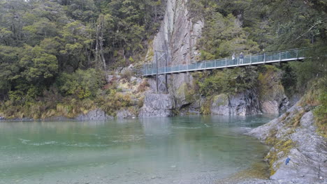 gente cruzando el puente en un lago verde y exuberante en nueva zelanda