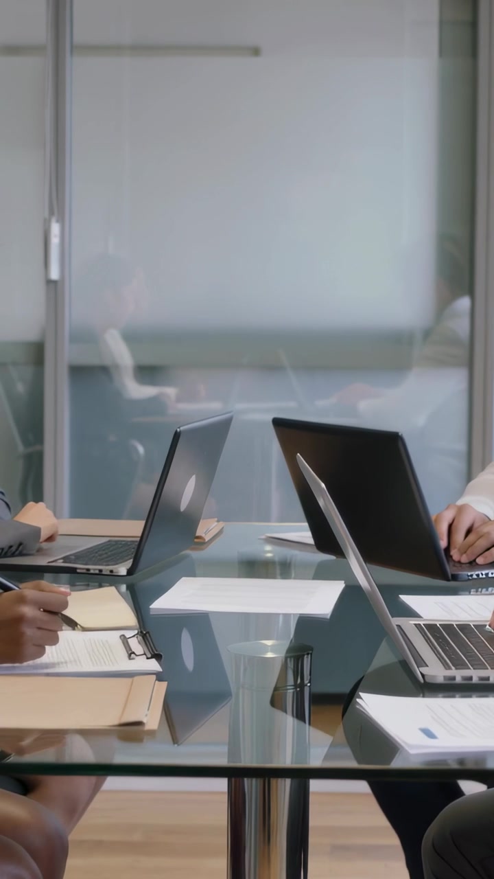 Video verticale: Laptop che si aprono, due colleghi che correggono documenti e digitano in una stanza di vetro, in abito