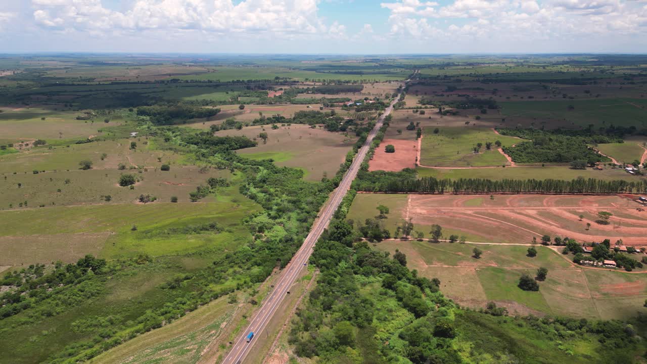 A wide aerial view of a long, straight highway or railway cutting through vast agricultural fields and natural riparian vegetation in the border region of São Paulo and Mato Grosso do Sul, Brazil