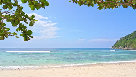 White-sand-beach-and-emerald-tranquil-sea-tides-in-tropical-laguna,-cloudy-sky,-tree-branches-in-the-foreground,-vacation-template,-copy-space-Minimalistic