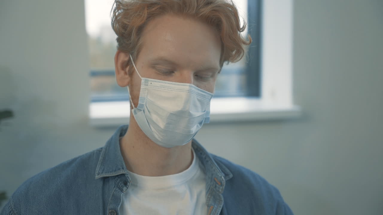 портрет молодого красивого рыжеволосого мужчины, разговаривающего по телефону с маской на лице в помещении