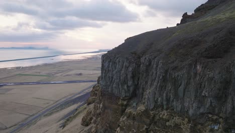 Aerial-panoramic-view-of-mountain-rock-formations-and-steep-cliffs,-with-melting-snow,-on-a-moody-evening-in-Iceland