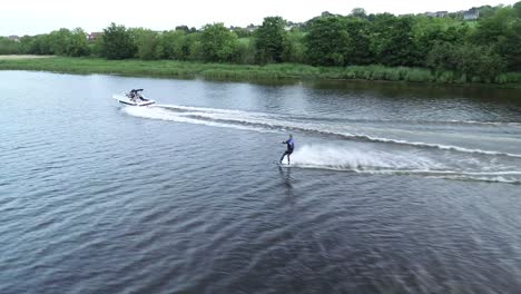 waterskiing in river bann, northern ireland uk, slow motion aerial view of skier and tow boat, tracking drone shot