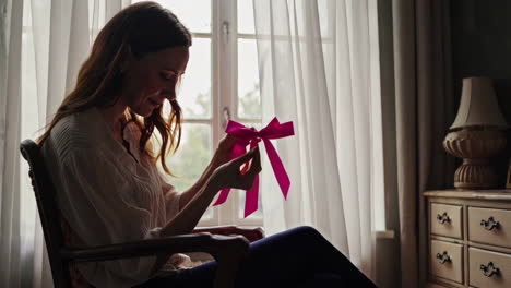 Woman Holding a Pink Ribbon by a Window