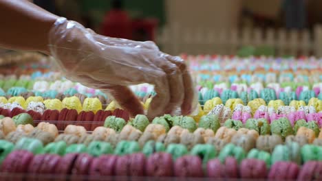 la mano del vendedor en un guante de plástico desechable que organiza coloridos macarons en filas