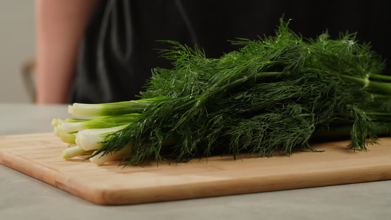 Cutting dill, chef cut dill with knife on a wooden board, close up at home, vitamin vegan greens.