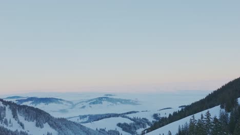 Mesmerizing-aerial-view-showcasing-the-tranquil-scene-of-a-snowy-mountain-range-silhouette-at-sunrise,-captured-by-drone