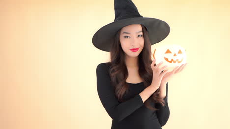 mientras sostiene una calabaza, una bruja sexy completa con sonrisas puntiagudas de sombrero negro