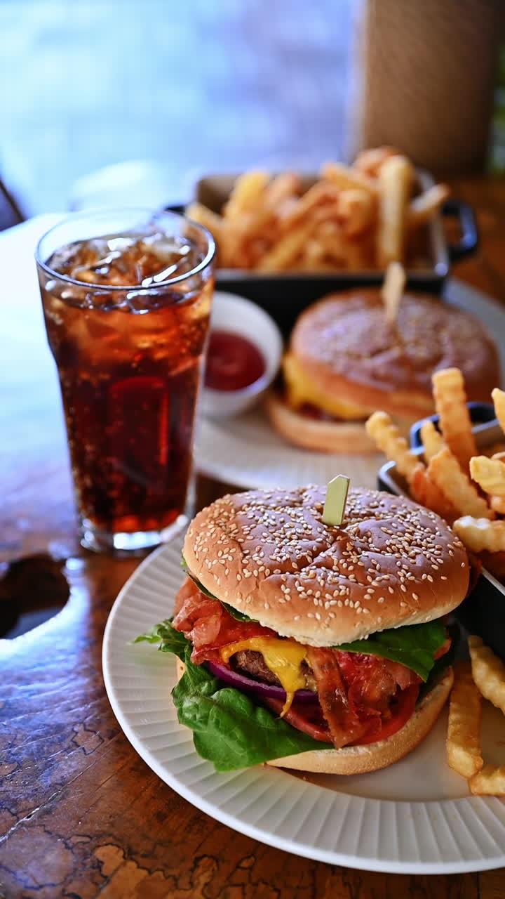 Cheeseburger with fries and cola on wooden table. Juicy cheeseburger with lettuce and bacon served with french fries and cola drink in restaurant setting