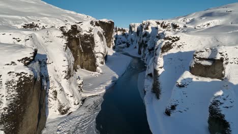 aerial view over a glacier river flowing through a canyon covered in snow, on a sunny day