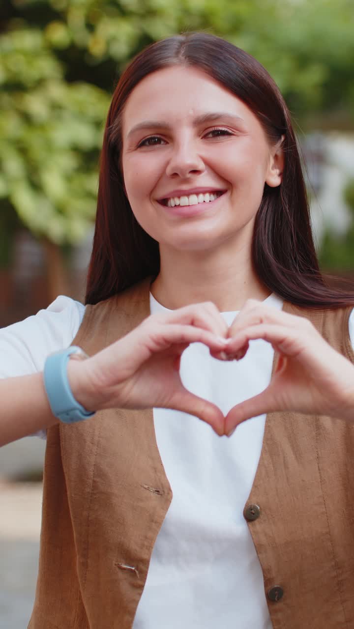 retrato de una joven caucásica hace un símbolo de amor mostrando un signo de corazón a la cámara en la calle de la ciudad
