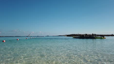 Beautiful-tropical-island-shoreline-with-paddle-boat-and-buoys-on-clear-warm-water