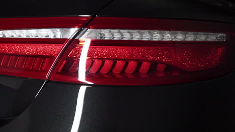 Ein-Lichtschimmer,-Der-Auf-Ein-Rotes-Rücklicht-Eines-Neuen-Luxuriösen-Schwarzen-Autos-Gleitet,-Das-Auf-Das-Heck-Des-Fahrzeugs-Scheint,-Zeitlupe-Mit-Nahaufnahme-Von-FHD