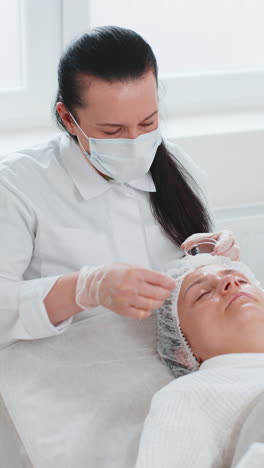 cosmetologist applying special moisturizing acid serum peeling face of caucasian woman in clinic