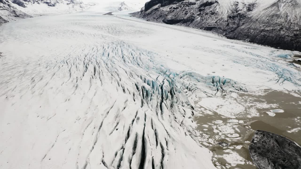 Drone footage showcasing the vast icy expanse of Svinafellsjokull glacier, surrounded by rugged peaks and meltwater lagoons.