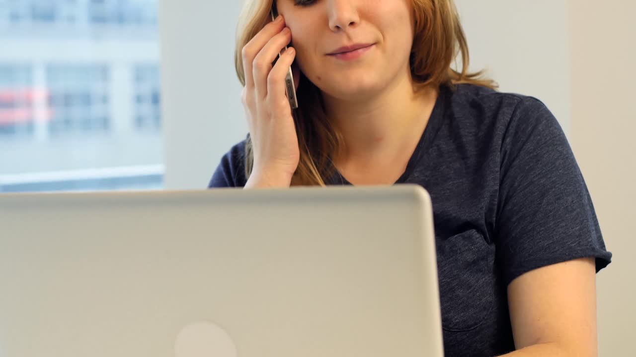 Kvinde, der bruger bærbar computer, mens hun taler i mobiltelefon