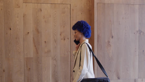 happy biracial businesswoman with blue afro talking on smartphone in office, slow motion
