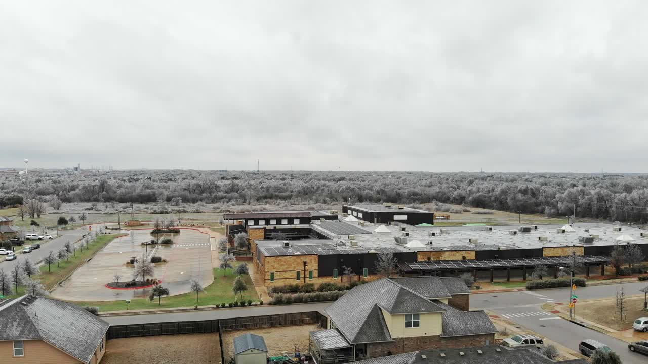 아래에 몇 개의 집이 있는 동네에서 날아나오고, 지붕에 많은 태양 전지 패널이 있는 초등학교 쪽으로 이동하고, 거대한  ⁇ 과 멀리 있는 얼어붙은 나무의 부분