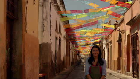 woman looking up at colorful papel picado banners decorating a narrow street