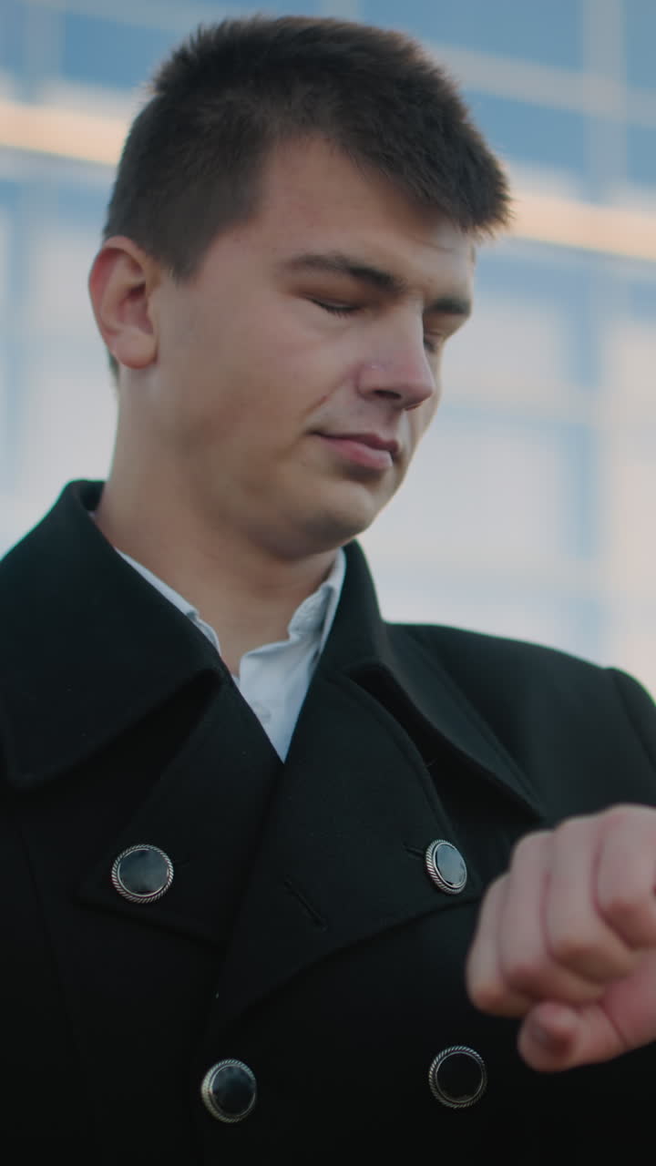 검은 옷을 입은 남자가 멀리 바라보는 동안 손목 시계를 확인하며 자신감과 결단력을 발산합니다.