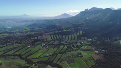 Aerial---Farms-from-above-looking-like-patches-stitched-together,-flying-sidewards---road-snaking-up-mountainside