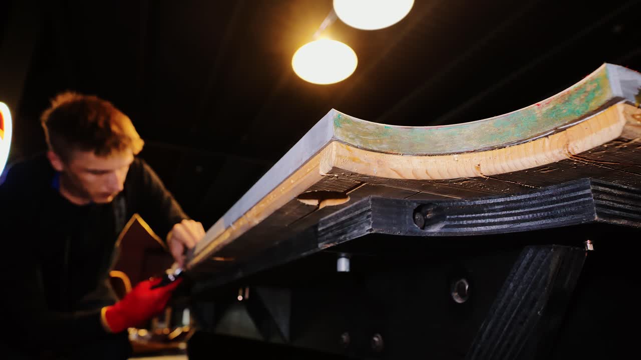 Close low angle, man pulling staples from pool table frame, warm yellow lights