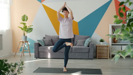mujer practicando la postura del árbol de yoga en casa
