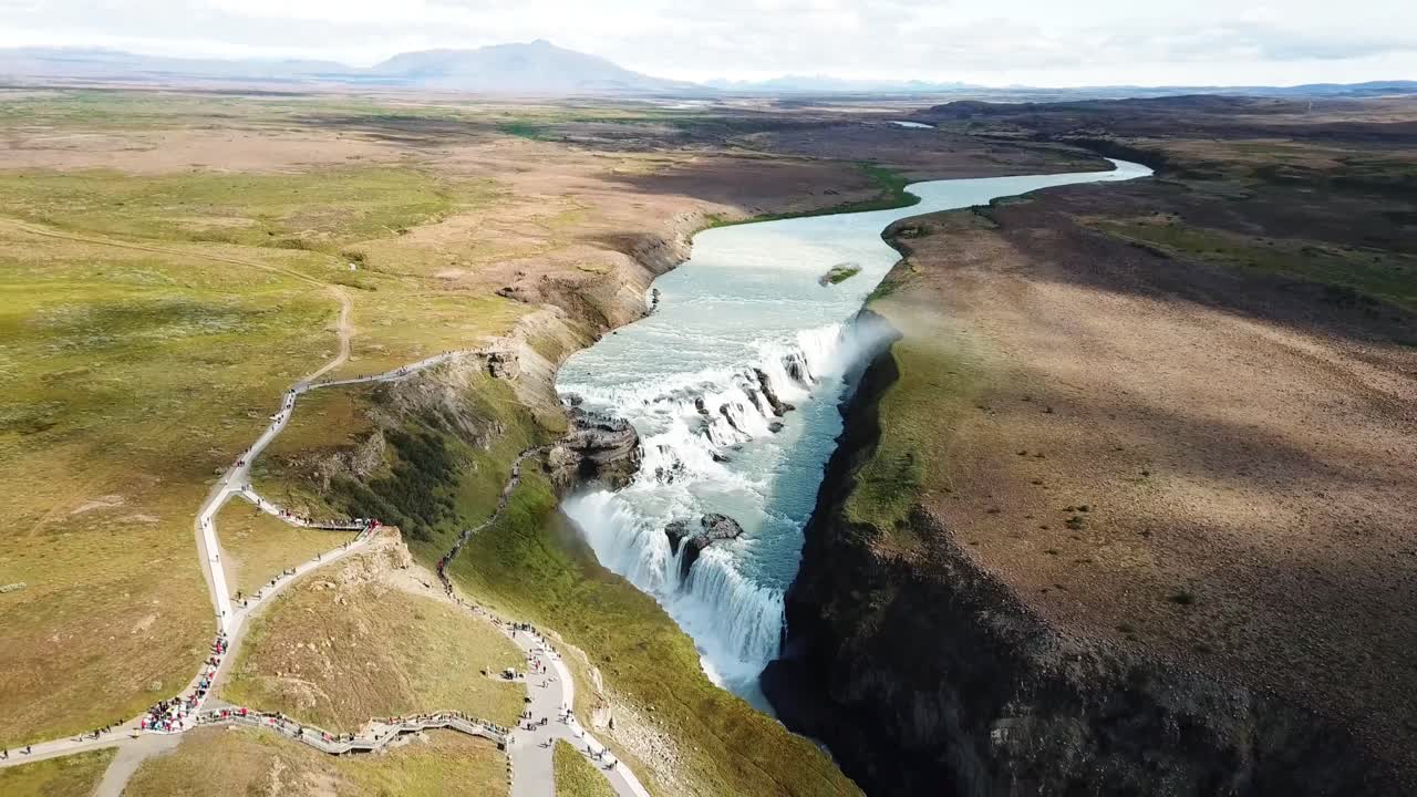 A stunning aerial view of Gullfoss waterfall in Iceland, surrounded by rugged terrain and a winding river, showcasing the power and beauty of nature in a dramatic setting