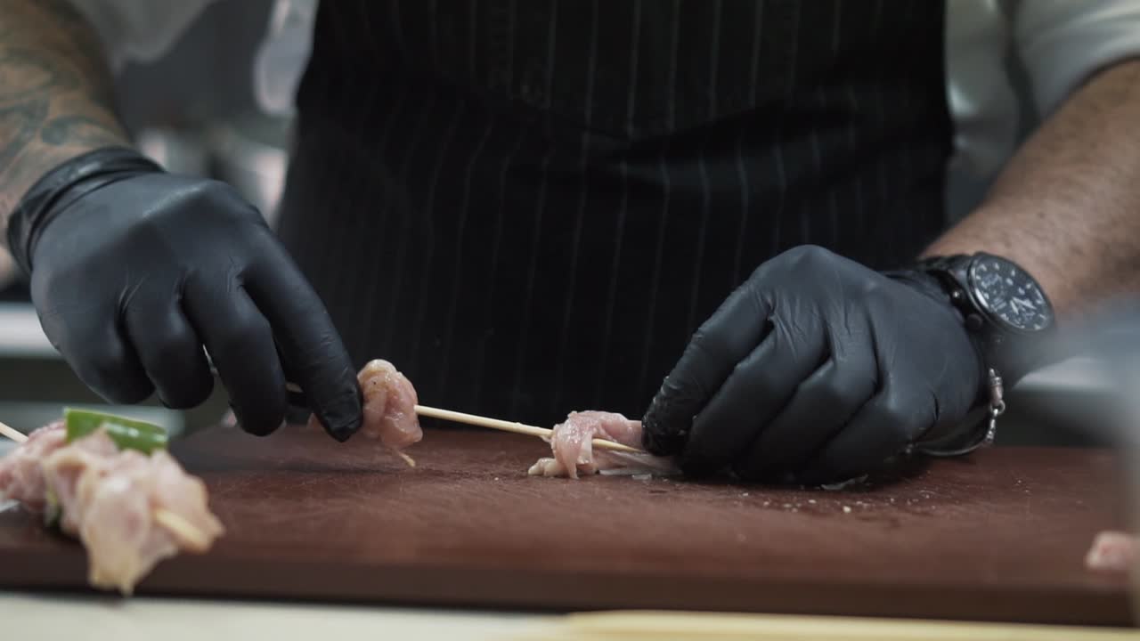 Master chef putting raw meat peaces on skewer for grilling