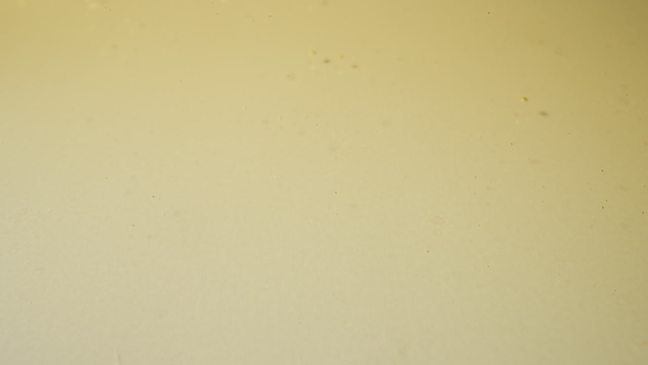 gotas de aceite de jojoba cayendo en un charco dorado haciendo salpicaduras