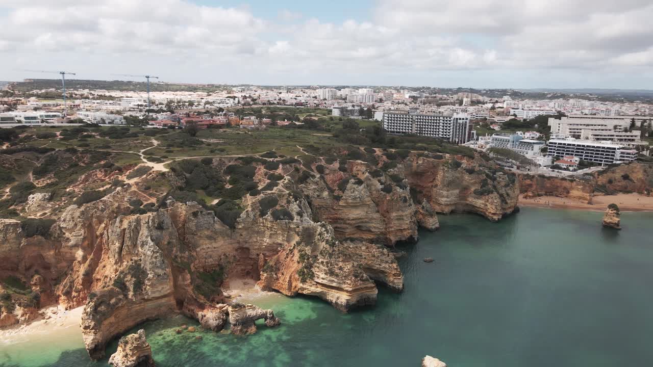 Aerial drone turns right from cliffs to wide view of Lagos city skyline and coastline in southern Portugal